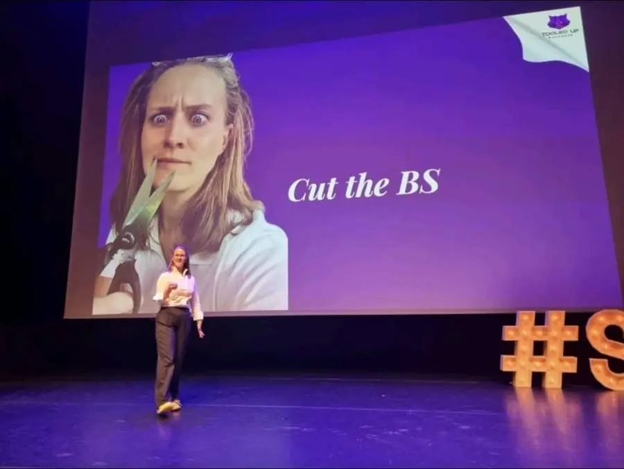 Gabi on stage, a screen behind her reading Cut the BS